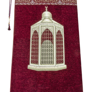 Un tapis rouge décoré d'un monument arabe est étendu sur un fond blanc. Il est orné de détails dorés et de franges blanches. Un chapelet de prière est posé sur la gauche.