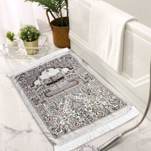 Tapis de prière en coton blanc avec un motif tissé de la kaaba. Le tapis est posé dans une salle de bain à côté d'une baignoire et de pots de fleurs