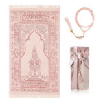 Un tapis de prière rose clair est étendu sur un fond blanc. Un chapelet assorti est à sa droite et une petite boîte cadeau.