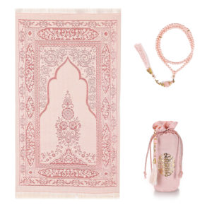 Un tapis de prière rose clair est étendu sur un fond blanc. Un chapelet assorti est à sa droite et une petite sacoche également.