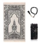 Un tapis de prière noir est étendu sur un fond blanc. Un chapelet assorti est à sa droite et une petite boîte cadeau.