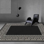 Un tapis noir avec des formes géométriques beige est installé au sol dans un salon très moderne. Les murs sont en béton gris, un cadre uni est sur le mur. Il est a une lampe noir suspendue et une chaise design complètement noire.