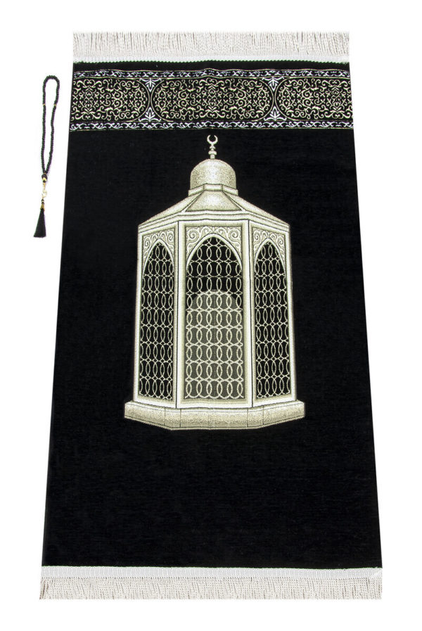 Un tapis noir décoré d'un monument arabe est étendu sur un fond blanc. Il est orné de détails dorés et de franges blanches. Un chapelet de prière est posé sur la gauche.