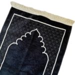 Un tapis noir est posé sur une fond blanc. Des motifs orientaux ornent le tapis et des franges sont visibles aux extrémités du tapis. Le motif ressemble à une porte d'entrée.