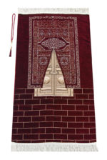 Un tapis rouge est étendu sur un fond blanc. Il est décoré avec le motif des portes dorées de la Kaaba et de franges en haut et en bas. Il est accompagné d'un chapelet de prière.