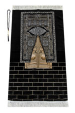 Un tapis noir est étendu sur un fond blanc. Il est décoré avec le motif des portes dorées de la Kaaba et de franges en haut et en bas. Il est accompagné d'un chapelet de prière.