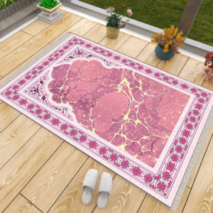 Tapis de prière rose effet marbre. Un tapis luxueux fait en coton et antidérapant. Le tapis est posé sur du parquet avec des chaussons à côté et des fleurs contre la baie-vitrée