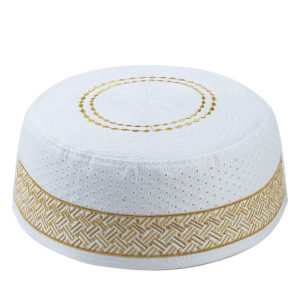 Un kufi rond et blanc sur fond blanc est décoré de broderies géométriques en fil doré.
