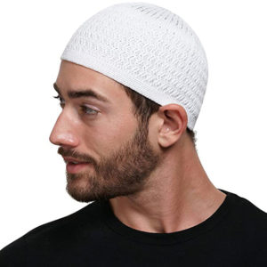 Un homme se tient de profil. Le fond est blanc et il porte une barbe. Il porte sur la tête un kufi blanc tricoté.