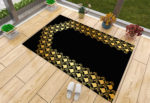 Un tapis de prière noir et doré posé sur du parquet à côté d'une fenêtre. Des chaussons sont posés à côté du tapis ainsi que des pots de fleurs. Le tapis est majoritairement noir avec une dorure en forme de porte.