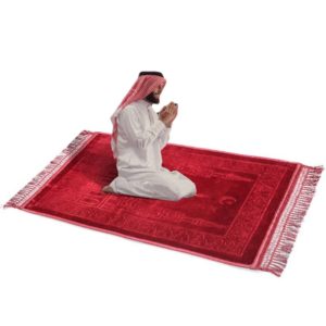 Superbe tapis de prière de taille large en velours rouge avec des motifs. Un homme habillé en blanc est en train de prier dessus
