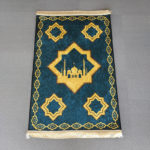 Tapis de prière en velours bleu à franges dorées. Le tapis est ornée d'étoiles à 8 branches avec une mosquée dans une étoile au centre.