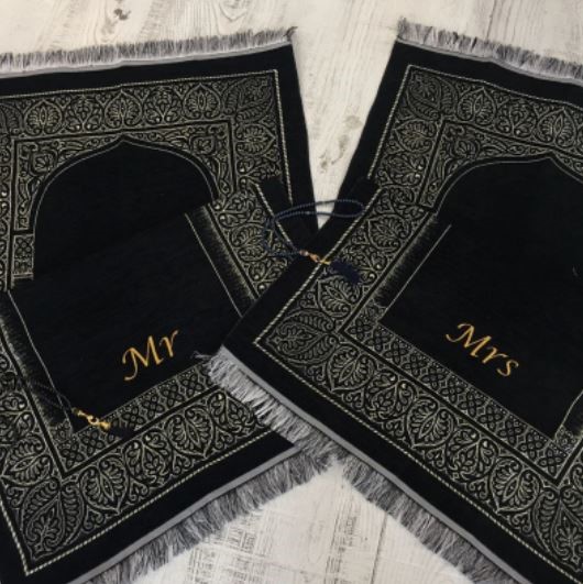 Deux tapis de prière noirs repliés sont sur le sol en parquet. Ils sont décorés de franges et de motifs orientaux. Mr et Mrs sont brodés sur les tapis assortis.