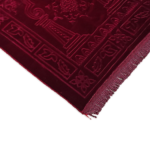 Un tapis rectangulaire rouge à franges est placé sur un fond blanc unis. Il est en velours.