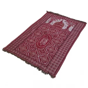 Ca tapis de prière est rouge et rectangulaire avec des motifs et un temps. Il est placé sur un fond blanc.