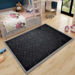 Tapis Rectangulaire à motifs noirs avec bordures blanches et à rayures. Le tapis est au milieu d'un chambre d'enfant. Il est placé entre un lit et une fenêtre.
