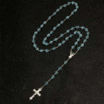 Chapelet catholique en perles bleu transparentes sur fond noir.