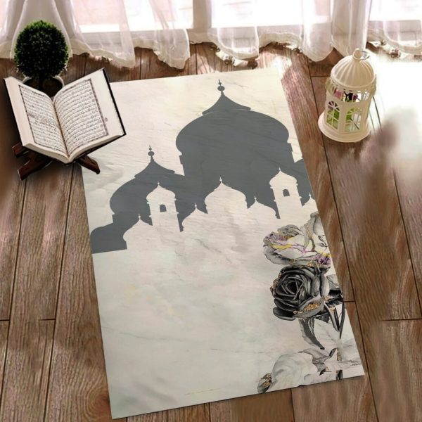 Un tapis de prière est étendue sur un sol en parquet. On distingue des ombres de bâtiments en motif sur le tapis. Un Coran est ouvert et une lampe est posée sur le sol.
