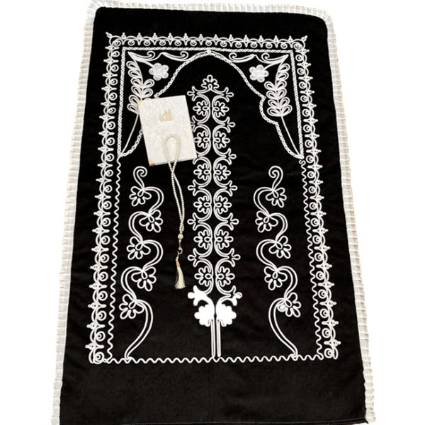 Tapis de prière en velours noir avec un fil banc brodé Le tapis a un contour en dentelle. Un coran et un chapelet sont pose sur le tapis
